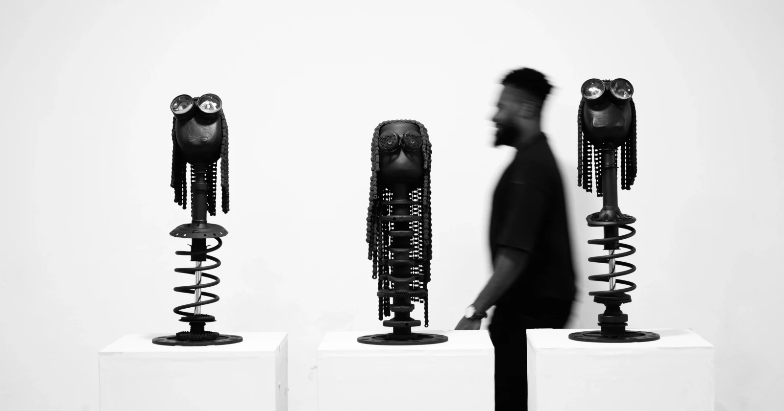 The artist walking past a row of his sculptures in a white gallery space